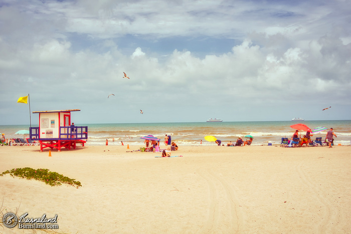 Seagulls fly overhead and ships sail along the horizon as people enjoy the sun at Cocoa Beach, Florida