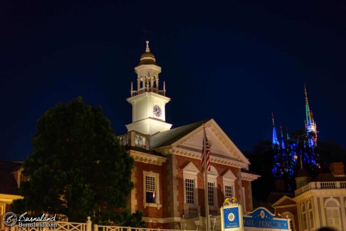 The Hall of Presidents in Liberty Square at night in the Magic Kingdom at Walt Disney World, with Cinderella Castle behind the trees at the right