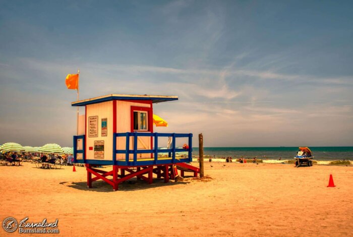 A yellow flag flies above the red, white, and blue lifeguard hut at Lori Wilson Park in Cocoa Beach, Florida