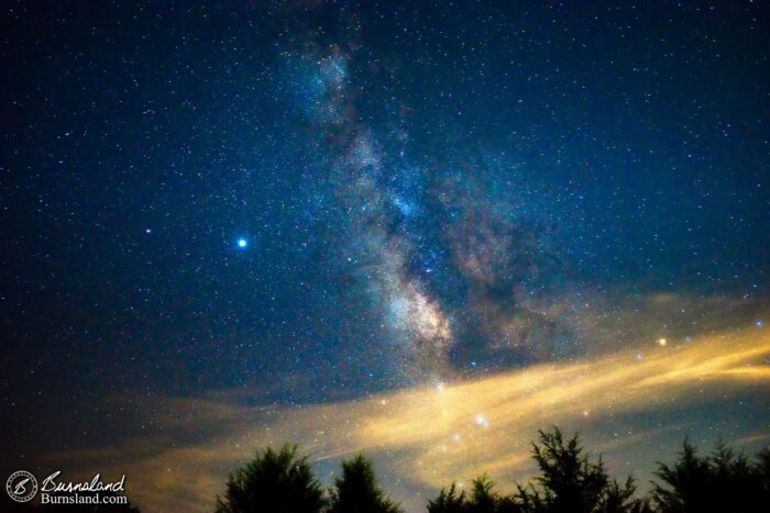 The Milky Way fills the sky above clouds and trees as seen from our backyard on a summer night. This fills me with a sense of wonder.