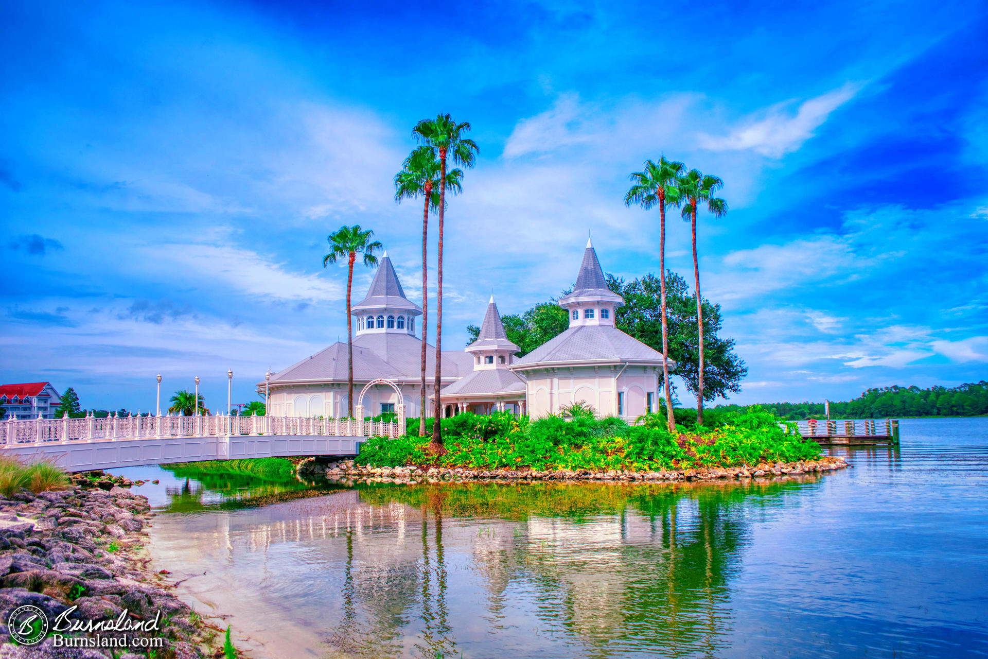 Disney’s Wedding Pavilion and the blue sky above are reflected in the waters of Seven Seas Lagoon at Walt Disney World