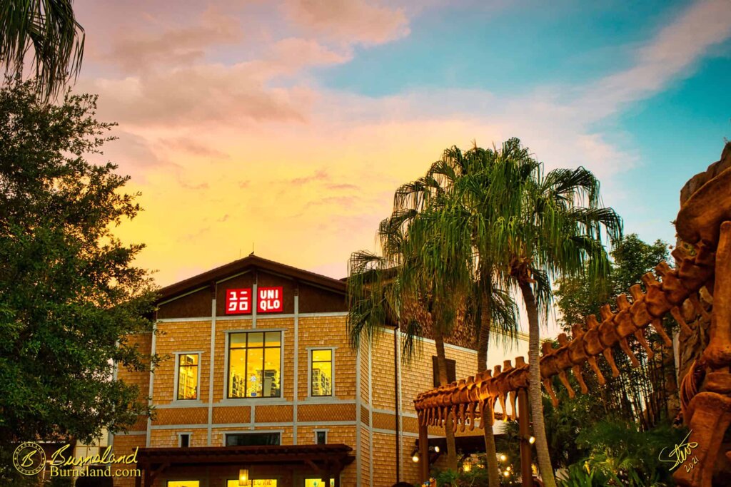 A colorful sunset sky above Uniqlo and the dinosaur fossil tail outside the T-Rex restaurant at Disney Springs in Walt Disney World.