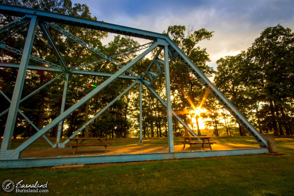 The sun sets through the trees and the supports of a bridge at Paris Landing State Park in Tennessee