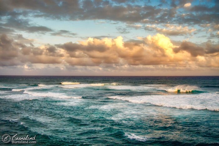 Waves roll in as the clouds part to reveal some blue sky in the evening at Shipwreck Beach on the island of Kauaʻi in Hawaiʻi