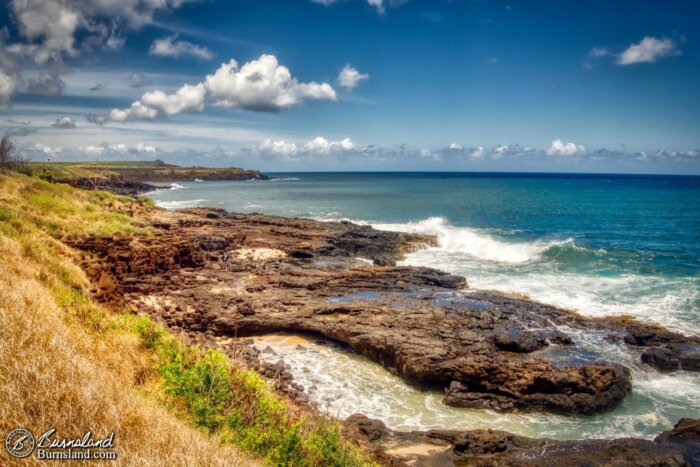 Waves roll onto the shore of lava rocks near Glass Beach on the island of Kauaʻi in Hawaiʻi